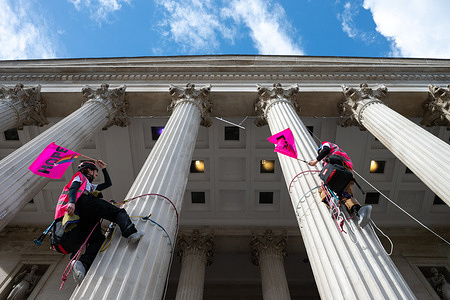 Two protesters seen waving flags during the rally. Two protesters climbed the columns of the National Gallery in Trafalgar Square during a march organized by Together Alliance and House Against Hate in central London against far-right movements and racism. The activists displayed flags reading “Hope” and “Love” as crowds gathered below, while police officers surround the base of the columns and prepare to make arrests.