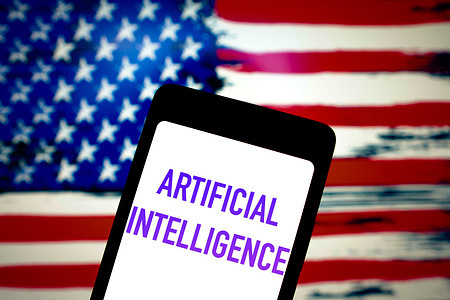 In this photo illustration, the Artificial Intelligence (AI) text is displayed on a smartphone screen and in the background, the flag of the United States. The United States government has issued an executive order that aims to control and regulate the risks posed by artificial intelligence technologies.
