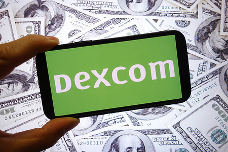 In this photo illustration, the DexCom company logo is seen displayed on a smartphone screen with United States dollar banknotes in the background.