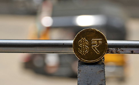 In this photo illustration, a chocolate coin wrapped in gold foil, featuring a Rupee and Dollar currency symbol, is displayed on an iron ledge. Indian rupee weakened against the US dollar largely reflecting the concerns prompted by the imposition of US tariffs rather than being a reflection of the Indian economy's fiscal position. US President Donald Trump tweeted that India and US are continuing negotiations to address the tariff issue between both countries.