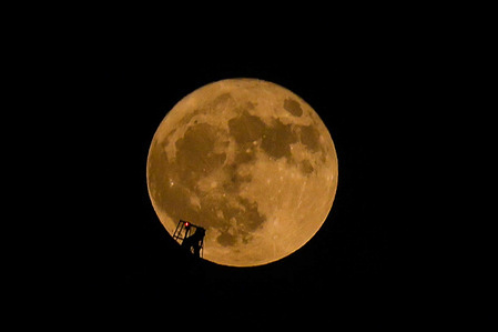 The full flower moon drifts passing in front of a construction crane.