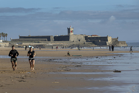 Two people are seen jogging on the sands of Carcavelos Beach in Lisbon. Carcavelos Beach is one of the most popular beaches along the Cascais coastline in Portugal. It combines a long stretch of golden sand bordering the Atlantic Ocean with a dynamic atmosphere marked by surfing and numerous outdoor activities.