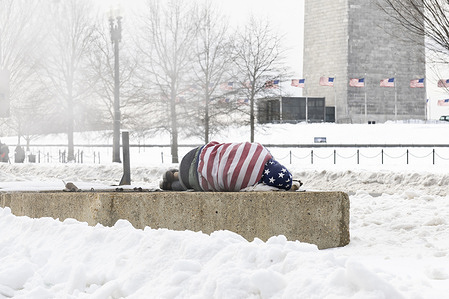 A homeless person rests on a warm air vent to stay warm following a heavy winter storm near the Washington Monument. The storm has brought frigid temperatures, ice, and heavy snowfall, leaving at least 10 people dead nationwide and causing widespread power outages affecting hundreds of thousands.