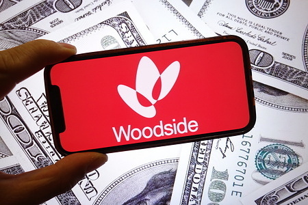 In this photo illustration, the Woodside Energy company logo is seen displayed on a smartphone screen with United States dollar banknotes in the background.
