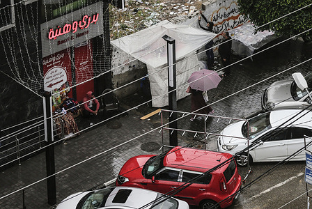 A Palestinian walking under an umbrella down the streets during a rainy day.