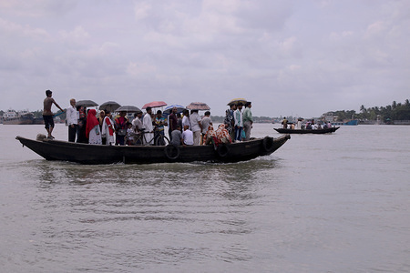 People cross a river with a wooden boat to go and work on an early morning in Khulna.