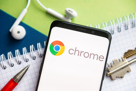 In this photo illustration, a Google Chrome logo seen displayed on a smartphone with a pen, key, book and headsets in the background.