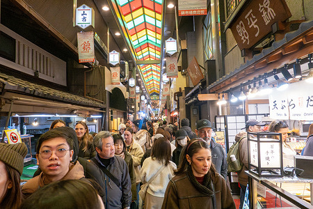Visitors crowd the narrow walkway of Nishiki Market, a historic covered shopping street lined with food stalls, shops, and traditional local specialties. Kyoto combines historic and contemporary elements, from the modern transport hub of Kyoto Station to traditional sites such as Shosei-en Garden. Seasonal cherry blossoms draw visitors each spring, while locations like Nishiki Market highlight the city’s culinary culture and daily life.