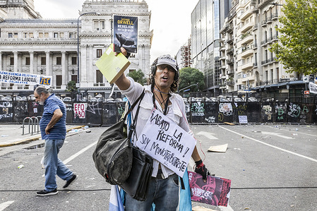 A protester wears a placard against the reform around his neck, raising a copy of George Orwell’s "Animal Farm" during the rally. Argentina’s Senate gave initial approval to a government-backed bill amid tense street protests that left at least 15 people injured and about 30 detained. By a vote of 42–30, lawmakers in the upper house passed a measure that seeks to dismantle the labor system in place, with amendments, since 1974.