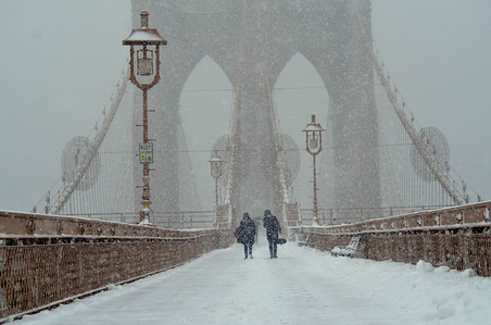 People are seen walking around Brooklyn bridge during a snowy day in New York City.