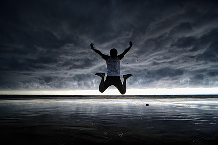 A man jumps as he poses for photos on the seaside of Udaipur Beach, Digha approximately 200 km from Kolkata with a dramatic cloudscape in the background. India Meteorological Department (IMD) has predicted that the Monsoon rain will likely arrive a week early this year due to twin cyclones, Asani and Karim.