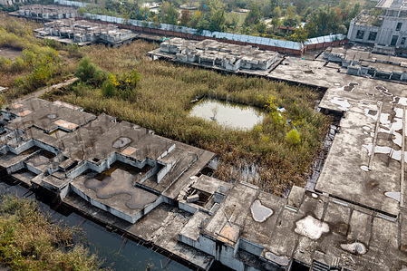 (EDITOR'S NOTE: Image taken by a drone) 
Aerial view of a large area of abandoned, unfinished concrete buildings with puddles on the roofs, surrounded by overgrown reeds and vegetation. The unfinished and abandoned buildings of the Evergrande Juntin project exemplify one of the many halted residential developments following the Evergrande Group’s insolvency. Once China’s second-largest property developer, Evergrande defaulted on debts exceeding $300 billion in 2021, triggering the suspension of countless pre-sold housing projects nationwide. These so-called “broken houses” have left thousands of Chinese homebuyers in financial and housing limbo, underscoring the severe impact of China’s ongoing real estate crisis.
