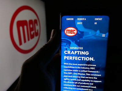 In this photo illustration, a person is holding a smartphone with the webpage of company MEC Mayville Engineering Company Inc. on screen in front of logo.