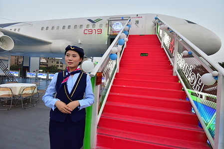 A staff member stands beside the red stairs leading to the aircraft - themed restaurant, with the plane in the background. The restaurant named "558 Aircraft Restaurant" has recently started its trial operation. This aviation - styled themed restaurant is renovated from a retired Boeing 737 aircraft, with the exterior painted in the livery of C919. The interior can accommodate 80 people for dining at the same time and is equipped with dining tables and soft and comfortable sofas.
