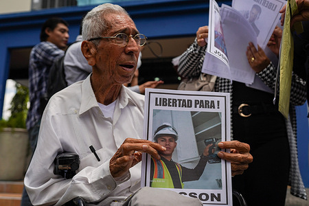 Walter Márquez, president of the Fundación El Amparo Internacional, a human rights organization, holds a picture of a detained Venezuelan migrant at the human rights ombudsman's office accompanied by relatives of Venezuelans deported by the United States to El Salvador. Relatives of two Venezuelans deported by the U.S. to El Salvador are urging the Bukele administration to allow visitation at the Center for Terrorism Confinement (CECOT), where 252 individuals are held. The deportees, mainly accused of gang ties to Tren de Aragua, were removed under the Alien Enemies Act, a move criticized by human rights groups and UN experts as unlawful and lacking due process. Critics argue the detentions are arbitrary, amount to enforced disappearances, and violate international law, especially since many detainees reportedly have no criminal records.