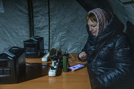 A woman charges her devices inside an emergency heating and power tent set up by the State Emergency Service of Ukraine to provide a heated shelter where people can charge their devices and have hot drinks on the left bank of Kyiv, Ukraine. Much of Kyiv is experiencing extensive power, heating, water and gas outages due to Russian attacks on Ukrainian infrastructure, as winter temperatures drop to -17C.