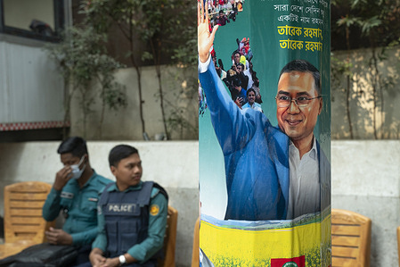 Police officers sit in the background behind a campaign placard depicting Tarique Rahman, the Chairman of the Bangladesh Nationalist Party (BNP). The poster promotes his candidacy for the upcoming general elections scheduled to be held on February 12, 2026, in Dhaka, Bangladesh.