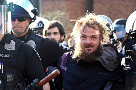 A man is led away by Seattle Police after being arrested while protesting a rally by the conservative group Patriot Prayer at the University of Washington. The rally went ahead after a federal judge blocked the university from billing organizers for event security. Fights erupted at various points during the dueling demonstrations. Credit: Toby Scott.