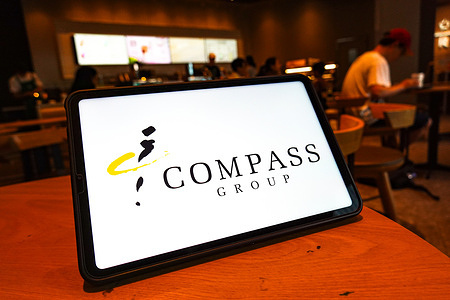 In this photo illustration, the Compass Group logo is displayed on the screen of a tablet.