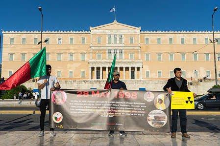 Protesters hold a banner, flags and a placard in front of the Greek parliament during a demonstration.
Protesters gathered in front of the Greek parliament to protest against nuclear tests in the area of Balochistan. On 28th of May 1998, Pakistan tested its first nuclear bombs, announcing itself as a nuclear power. The nukes took place in Changai hills of Balochistan and the impact from radiation to the residents of the area was huge.