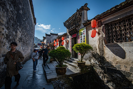 A narrow street in Xidi Village seen with Hui-style architecture, red lanterns and potted plants. Xidi Village is a renowned ancient village listed as a World Heritage Site by UNESCO. It showcases the exquisite Hui-style architecture with its white walls, gray tiles, and intricate carvings offering a vivid glimpse into traditional Chinese rural life. As a well-preserved example of ancient villages in southern China, Xidi attracts numerous visitors worldwide who come to appreciate its historical charm, cultural heritage, and picturesque scenery.