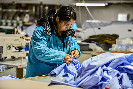 In the shirt production workshop of Anhui Baozitou Garment Co., Ltd., a female worker focuses on handling the fabric of a light blue striped shirt.