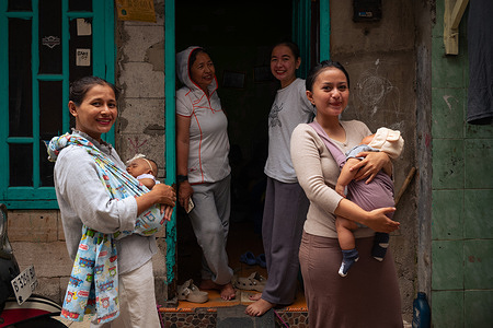 Indonesian women carrying babies stand in an alley in northern Jakarta.