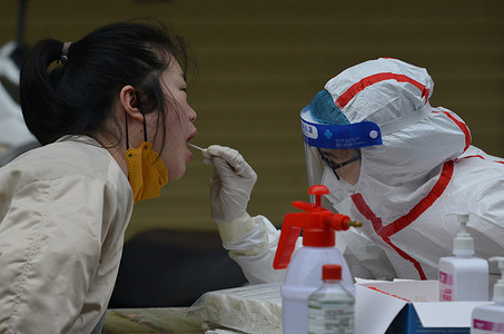 A healthcare worker wearing protective gear, takes a mouth swab sample from a resident for COVID-19 testing at a controlled area in Fuyang. The Chinese mainland on Tuesday reported 1500 locally transmitted confirmed COVID-19 cases, the National Health Commission's Wednesday report showed. Of the new local confirmed cases, 1189 were reported in Shanghai.