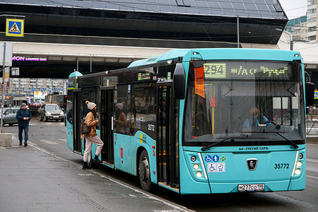 Passengers board on a blue passenger bus at a public transport stop on Testers Avenue, near the metro stations Komendantsky Prospekt and Pionerskaya.