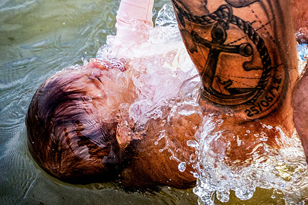 A man holds a young child underwater during the Holy Bath ritual, believed to protect children from fear and illness. The annual tradition draws families to the Atlantic coast.