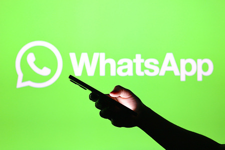 In this photo illustration, the WhatsApp logo seen in the background with a silhouette hand holding a smartphone.