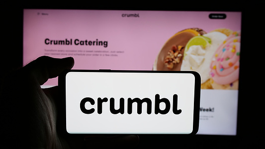 In this photo illustration, a cellphone with the logo of US bakery chain company Crumbl LLC is seen on screen in front of webpage.