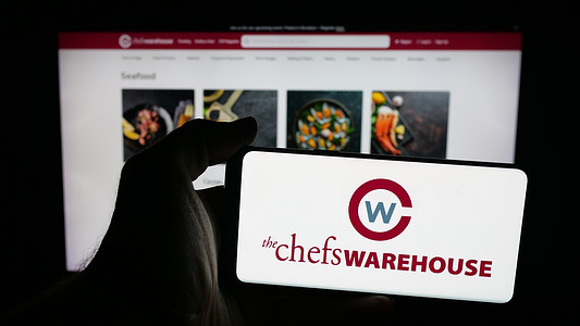 In this photo illustration, a mobile phone with the logo of US food company The Chefs Warehouse Inc. is seen on screen in front of web page.