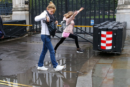 A young girl leaps over a puddle of rain water following overnight rainfall at the gates of Houses of Parliament in Westminster. More rain is expected in the coming days.