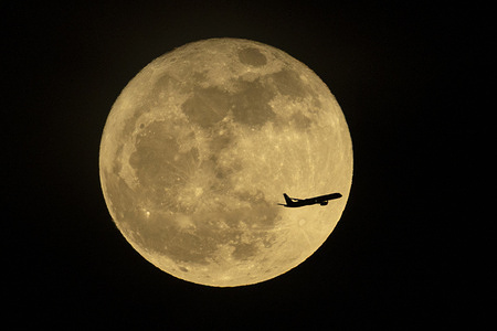 An airplane flies past the full moon, also known as the Flower Moon, rising over Los Angeles.