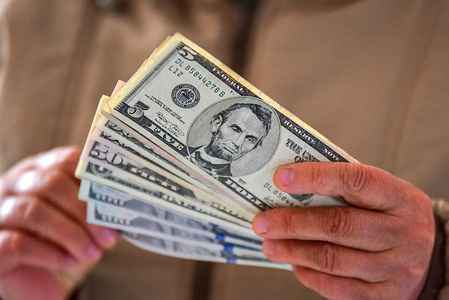 In this photo illustration, a hand fans out U.S. dollar bills, with a $5 bill (featuring Abraham Lincoln) prominently visible at the top. The US Federal Reserve on Wednesday decided to lower the target range for the federal funds interest rate by 25 basis points to 3.5 to 3.75 percent, marking its third rate cut this year.