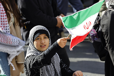 A girl waves an Iranian flag during the protest. A protest took place in Melbourne, with demonstrators marching to the U.S. Consulate to denounce American foreign policy concerning both Palestine and Iran. Participants demanded an end to U.S. military support for Israel amid the Gaza war and condemned recent American airstrikes on Iranian nuclear sites carried out in coordination with Israel since June 2025 which have intensified regional tensions and raised concerns over possible retaliation.