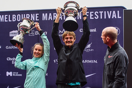 Caitlin Adams (L) and Jack Rayner (C) are seen holding up Melbourne Marathon trophies with Steve Moneghetti (R) looking at them during medal ceremony of Nike Melbourne Marathon at MCG Stadium.