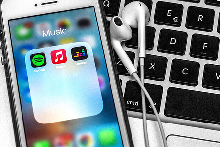 In this photo illustration a Spotify app, Apple Music app and Deezer app are seen displayed on a smartphone with headphones on a laptop keyboard.