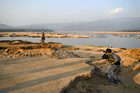 A photographer is seen taking photos of a sand and stone extraction laborer on the broken bank of the Jadukata River in Tahirpur, Sunamganj, Sylhet.