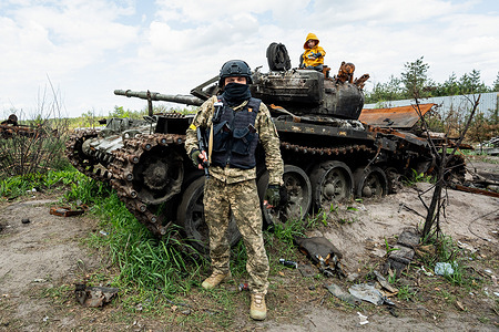 A soldier (who refused to give his name due to issues of personal safety) who fought where this destroyed Russian tank is located posing with his son who is on the tank.