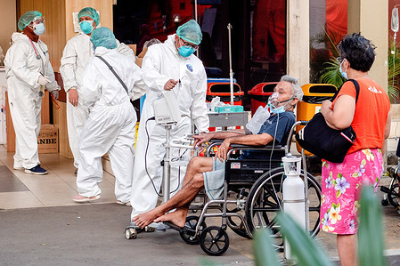 A healthcare worker wearing a personal protective equipment suit (PPE) attends to a COVID-19 patient with an oxygen mask in a wheel chair outside Bekasi Public Hospital.Hospitals in Java, Indonesia are shifting medical emergency units to tents outside hospitals to create more room for COVID-19 beds.