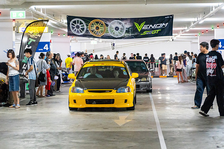 A yellow and black modified Honda Civic hatchback arrives at the car park of Terminal 21 Rama 3 in Bangkok, beneath a Venom advertisement banner, during the Bangkok Underground Riverside 2026 Car Meet. Bangkok Underground Riverside 2026 Car Meet, themed “The Fast Tokyo Drift,” brought together modified cars and automotive enthusiasts at Terminal 21 Rama 3, Car Park Level 4, in Bangkok. The event celebrated Bangkok’s underground car culture and street-style aesthetics, in the spirit of Tokyo’s drifting scene.