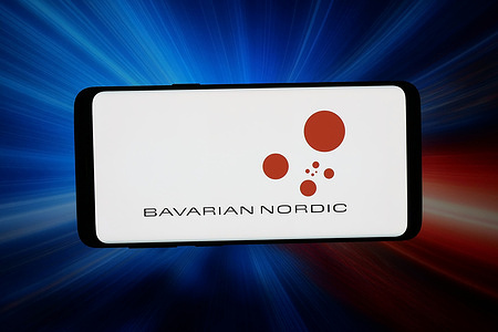 In this photo illustration, the logo of biotechnology company Bavarian Nordic AS is seen displayed on a smartphone in front of an abstract background on a computer screen.