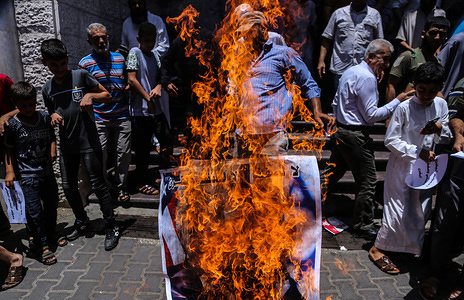 Palestinians burn a poster depicting U.S. President Donald Trump during the protest against Bahrain workshop for US peace plan in Gaza.