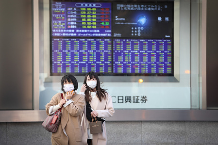 Women wearing face masks as a preventive measure against the spread of Covid-19 stand at a cross road in front of an electronic board showing Japan’s Nikkei 225 index and other indexes at a securities firm in Tokyo.