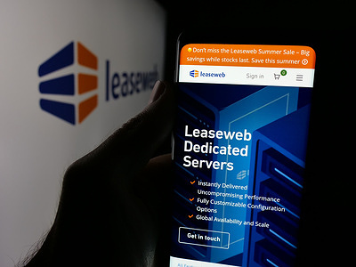 In this photo illustration, a person is holding a cellphone with the webpage of cloud computing company Leaseweb on screen in front of logo.