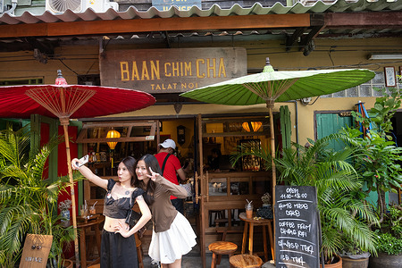 Girls pose for photos outside the popular Baan Chim Cha Cafe in Talat Noi. Talat Noi or Talad Noi meaning “Little Market” is a vibrant historical neighbourhood on the edge of Bangkok’s Chinatown. With a mixture of Thai and ethnic Chinese communities, traditional architecture and trendy cafes as well as car and motorcycle workshops, the area is rapidly becoming a popular destination for tourism, street photography and social media influencers.