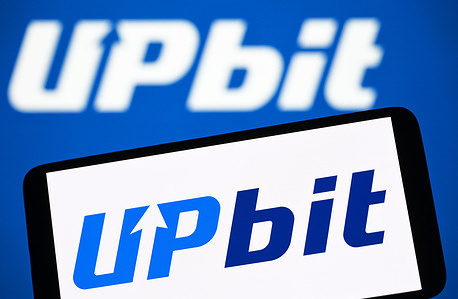 In this photo illustration, the Upbit logo is seen on a smartphone and in the background.