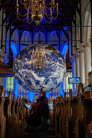 A woman is seen playing the cello in front of a big Earth ball. Gaia is a touring artwork by UK artist Luke Jerram. Measuring seven meters in diameter and created from 120dpi detailed NASA imagery of the Earth surface, the artwork provides the opportunity to see our planet, floating in three dimensions. This experience gives people a sense of awe, a deep realization of the interconnectedness of life on Earth. In Greek mythology, Gaia is the personification of Mother Earth. This artwork belongs to Arcadia, a 100-day cultural program that is taking place this summer in the province of Friesland, The Netherlands.